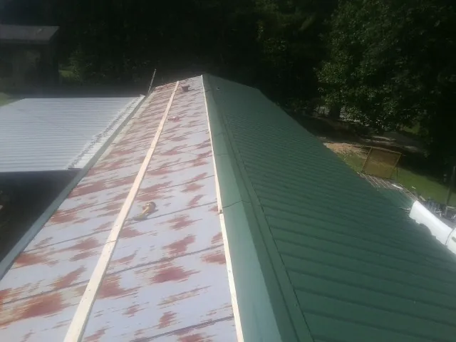 Old rusted panels beside newly installed green metal roofing — Wind Damage Roof Repair by Roofing Brothers in Cordova